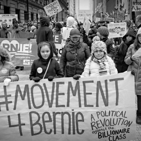black and white photo of marchers holding a banner that reads "#movement4bernie"