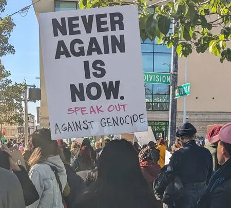Protester holding sign that reads, "Never again is now. Speak out against genocide."